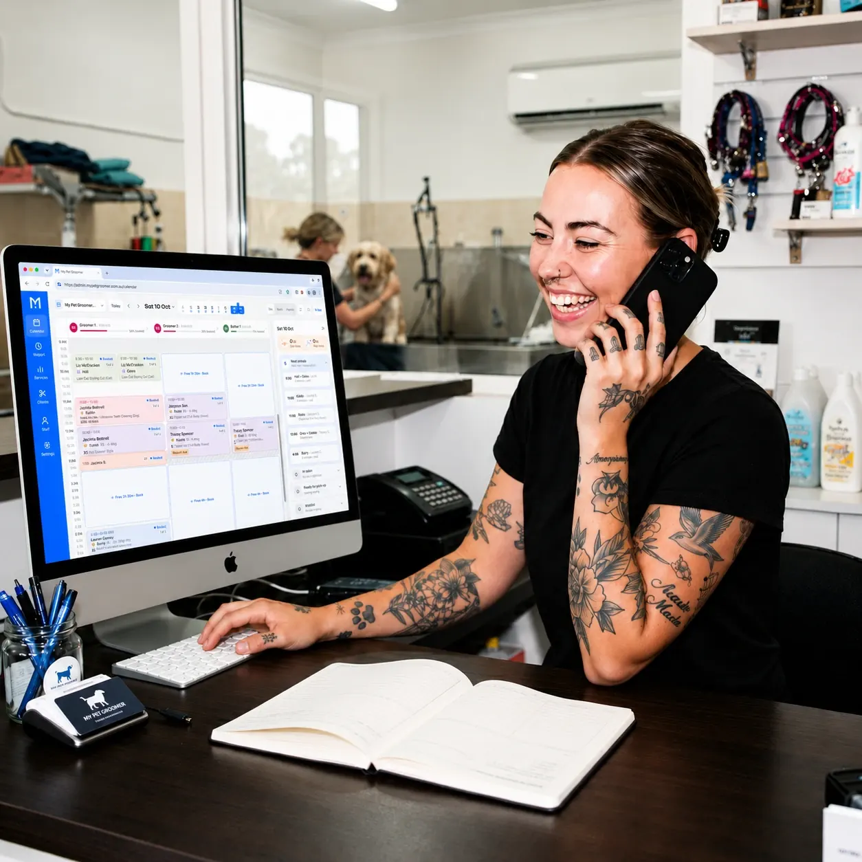 A groomer at the front desk taking a booking on the phone, with My Pet Groomer's calendar on screen